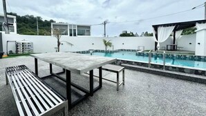 A rooftop pool area with a table and benches, surrounded by a white wall and a modern building in the background. - Luxury 5BR Home w/ Private Pool, 18Pax, Netflix (Langkawi)