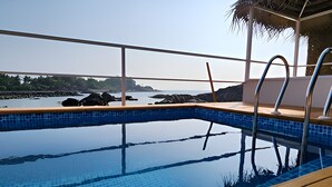 A clear view of a swimming pool with a tiled edge, a wooden deck, and a metal railing. - Destiny Goa Beach Resort (Canacona)