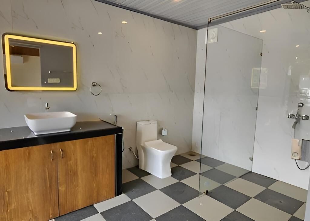 A bathroom with a black and white checkered floor, a white sink with a wooden cabinet, a white toilet, and a glass shower enclosure.