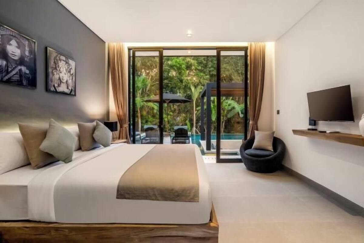 Ein modernes Schlafzimmer mit einem großen Bett, einem Fernseher und Blick auf einen Swimmingpool.