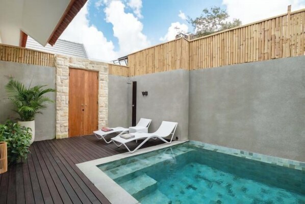 A modern outdoor pool area with two lounge chairs, a wooden fence, and a stone wall. - Villa Serenya Ubud (Bali)