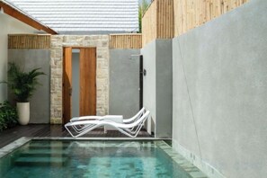 A swimming pool with lounge chairs, a wooden door, and a stone wall. - Villa Serenya Ubud (Bali)