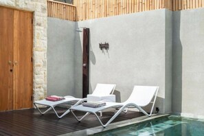 A pool area with two lounge chairs and a wooden door. - Villa Serenya Ubud (Bali)