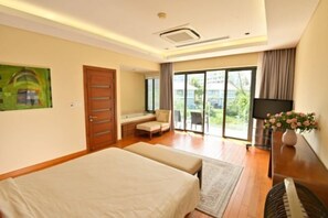A hotel room with a bed, a seating area with a sofa and armchair, a television, and a large window with a view of greenery. - Private pool villa - Your home, your resort (Da Nang)