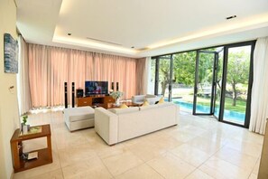 A spacious living room with a large sofa, a TV, and a glass door leading to a balcony. - Private pool villa - Your home, your resort (Da Nang)