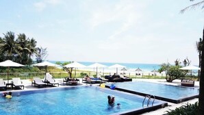 A pool area with lounge chairs and umbrellas, overlooking a beach. - Private pool villa - Your home, your resort (Da Nang)