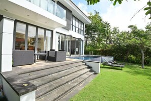 Una casa moderna con piscina, mobiliario exterior y un césped bien cuidado.
