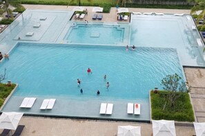 Una amplia piscina al aire libre con múltiples carriles, rodeada de sillones de descanso y sombrillas.