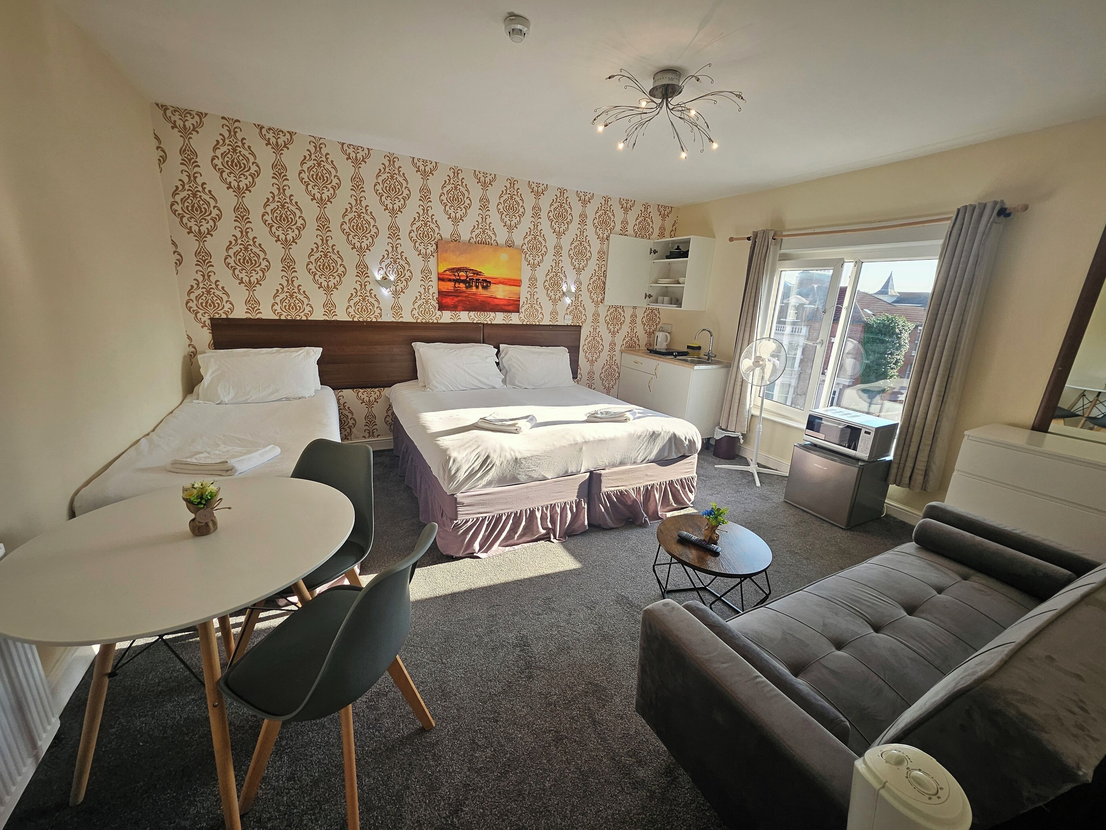 A hotel room with a bed, a desk, a chair, a sofa, and a large window.