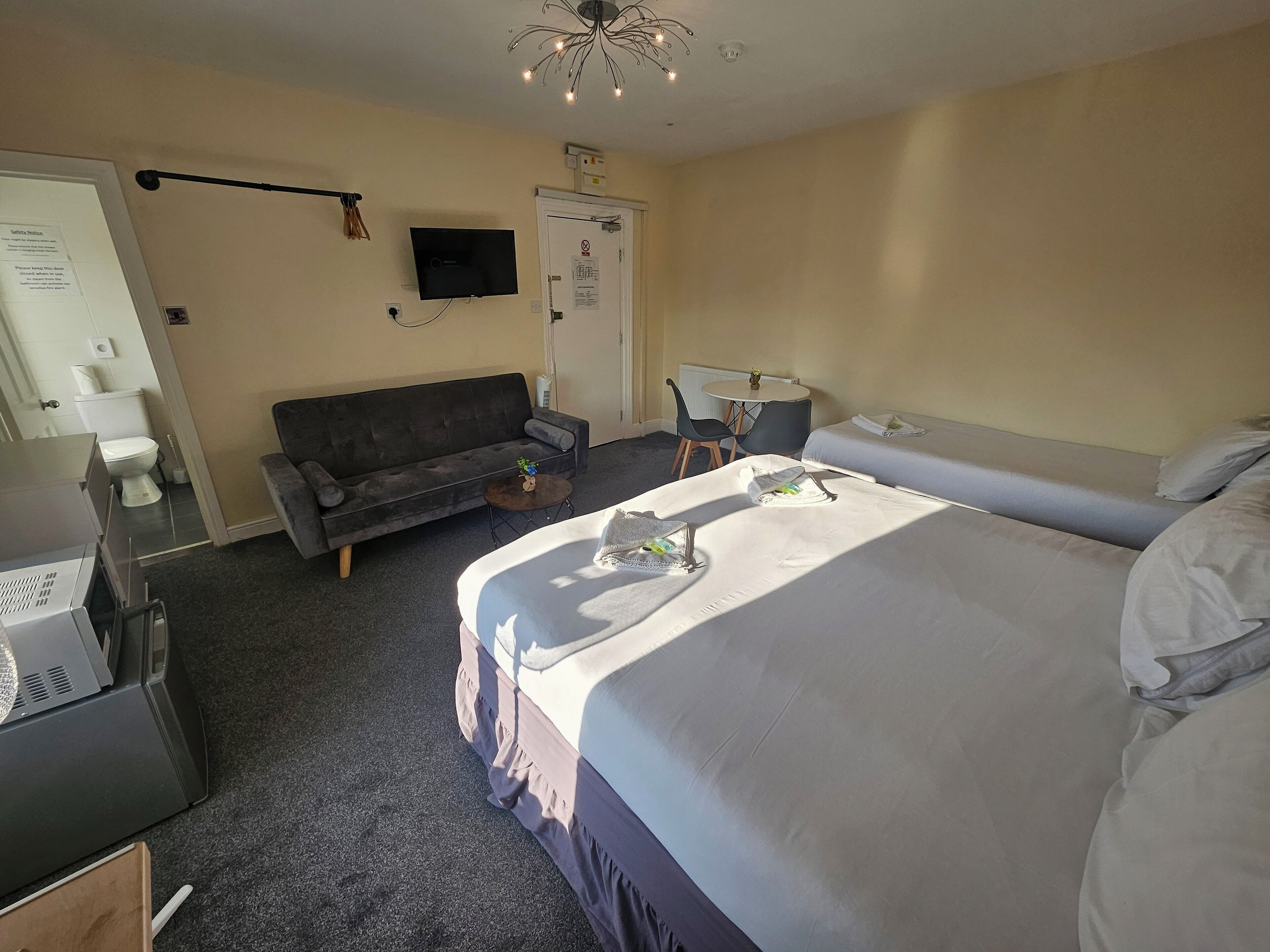 Una habitación de hotel con cama, sofá, una mesita, televisor y puerta.