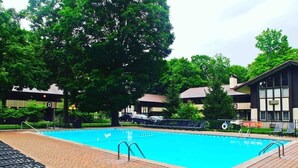 Una piscina con borde de baldosas, rodeada de árboles y edificios.
