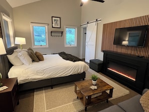 A bedroom with a bed, bedside tables, a TV, a fireplace, and windows. - Coming for a short trip but don't want to stay in a hotel room? Stay Downhill. Comfy, cozy and the feel of home! Kitchenette stocked with essentials to make a quick meal. Extra comfortable bedding and lounging areas. <br>Walking distance to ski lift. (Boyne Falls)