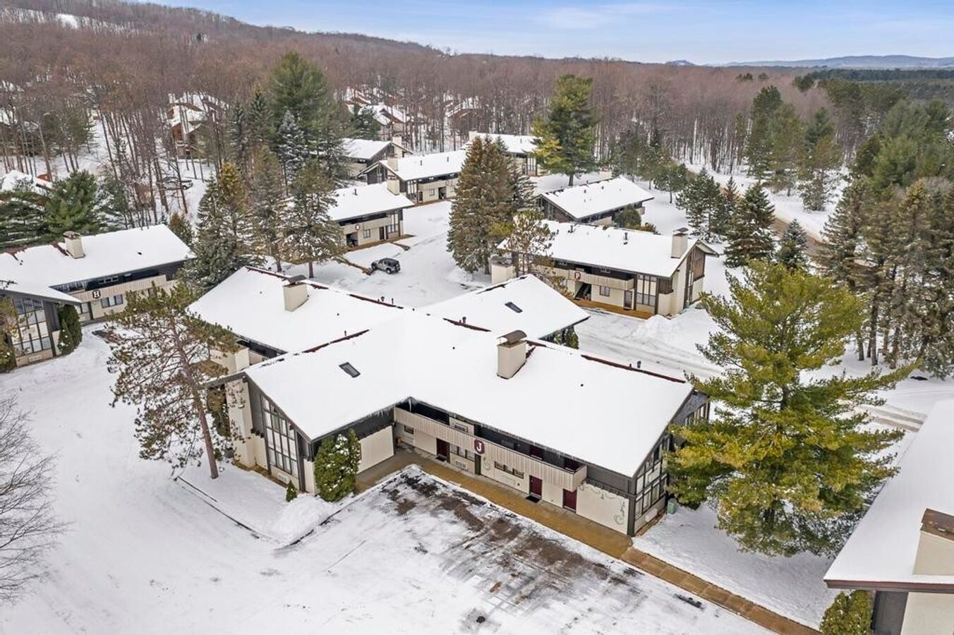 A snow-covered residential area with modern houses, surrounded by trees and hills.