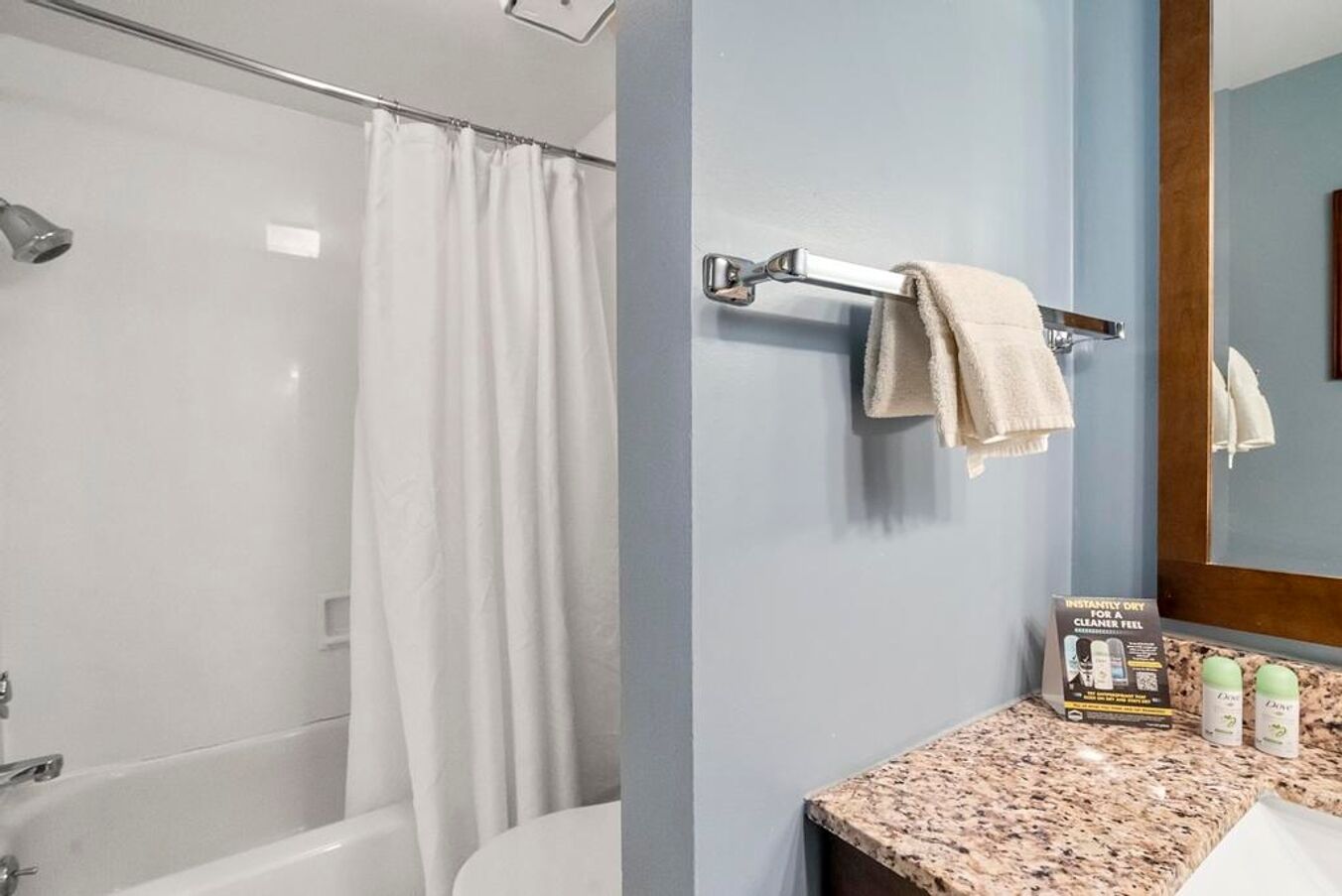 A bathroom with a shower, a bathtub, a sink with a granite countertop, and a towel rack with two towels.