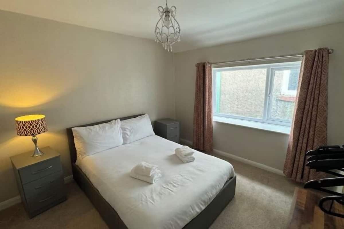 A hotel room with a bed, bedside lamp, dresser, and a window with curtains.