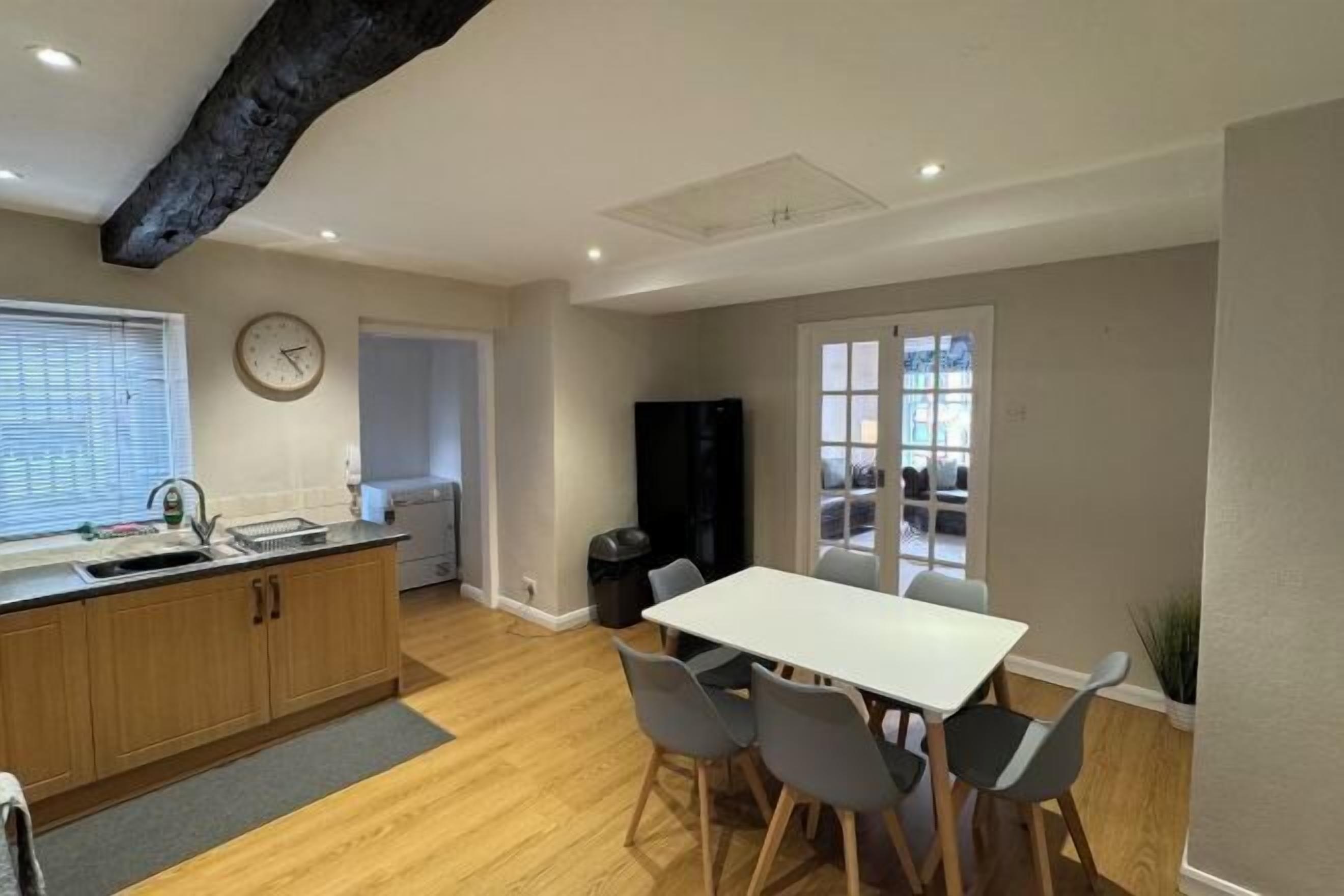 A modern kitchen with wooden cabinets, a white countertop, and a dining area with a white table and grey chairs.