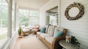 Una habitación acogedora con un sofá de mimbre, una mesita y una silla. Hay un adorno circular en la pared y una ventana con vistas a la vegetación.