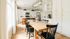 Una cocina moderna con armarios blancos, una mesa de comedor de madera, sillas negras e iluminación colgante.