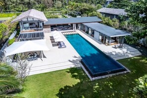 Una casa moderna con piscina, mobiliario exterior y un porche cubierto.