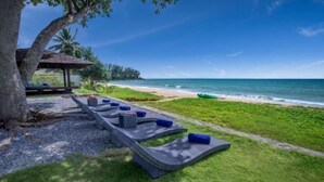 A beachside lounge area with a thatched-roof structure, a row of lounge chairs, and a view of the ocean. - Sava Villa 3 Villa Cielo (Takua Thung)