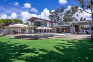 Una casa moderna con piscina, mobiliario exterior y un patio cubierto.