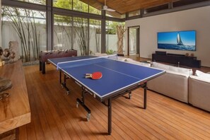 Una mesa de ping pong en una habitación con televisor, sofá y suelo de madera.