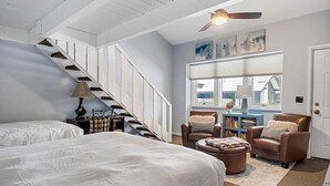 Un dormitorio con una cama grande, una silla, una mesita, una estantería y una ventana con persianas.