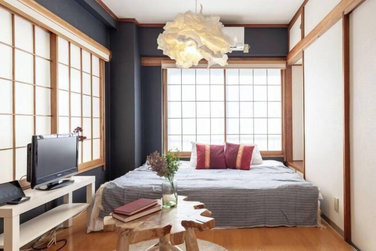 A Japanese-style bedroom with a bed, a TV, a desk, and a large window with traditional shoji screens.