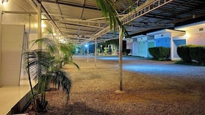 A covered outdoor area with a gravel path, palm trees, and a row of buildings with garage doors. - Fasuay Resort (Chatturat)