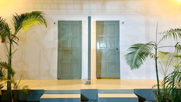 A hotel entrance with two glass doors, a white brick wall, and potted plants. - Fasuay Resort (Chatturat)