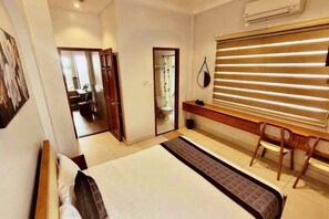 Une chambre avec un grand lit, un bureau et une chaise. Une porte donne accès à une salle de bain et à un couloir.