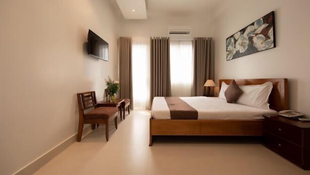 Une chambre d’hôtel comprenant un lit, une table de chevet, une lampe, une télévision et un bureau avec une chaise.