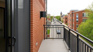 A balcony with a metal railing, a brick building, and a street view in the background. - Upscale 2-bedroom luxury loft in vibrant downtown Columbia, MO, in The District (Columbia)