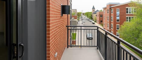 A balcony with a metal railing, a brick building, and a street view in the background.