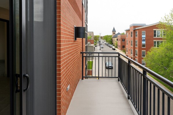 Un balcon avec une rambarde en métal, un bâtiment en briques et, au fond, une vue sur la rue.