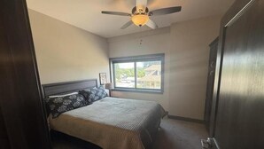 Un dormitorio con cama, ventilador de techo, ventana y puerta.