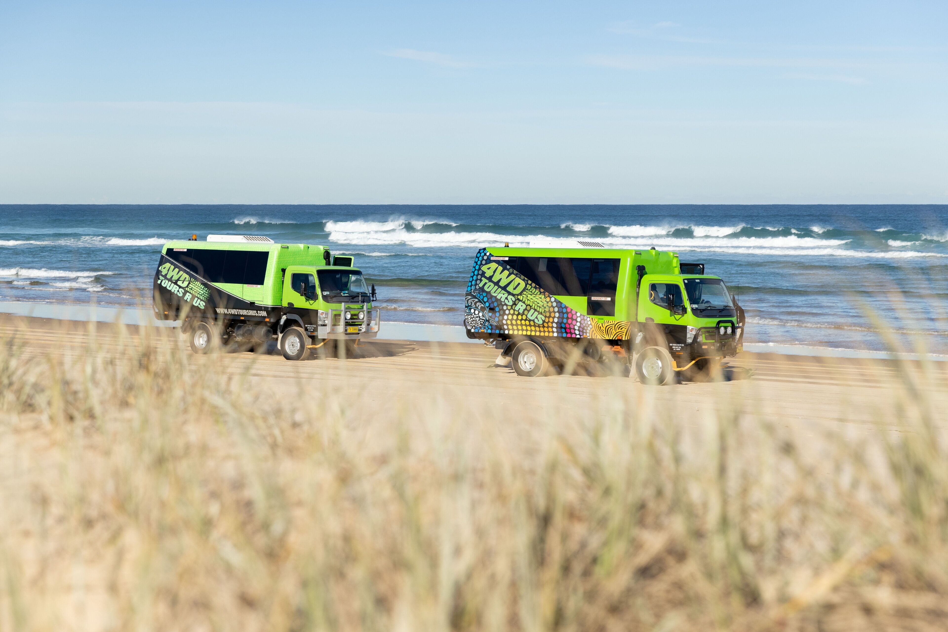 Two green tour vehicles parked on a beach with the ocean in the background.