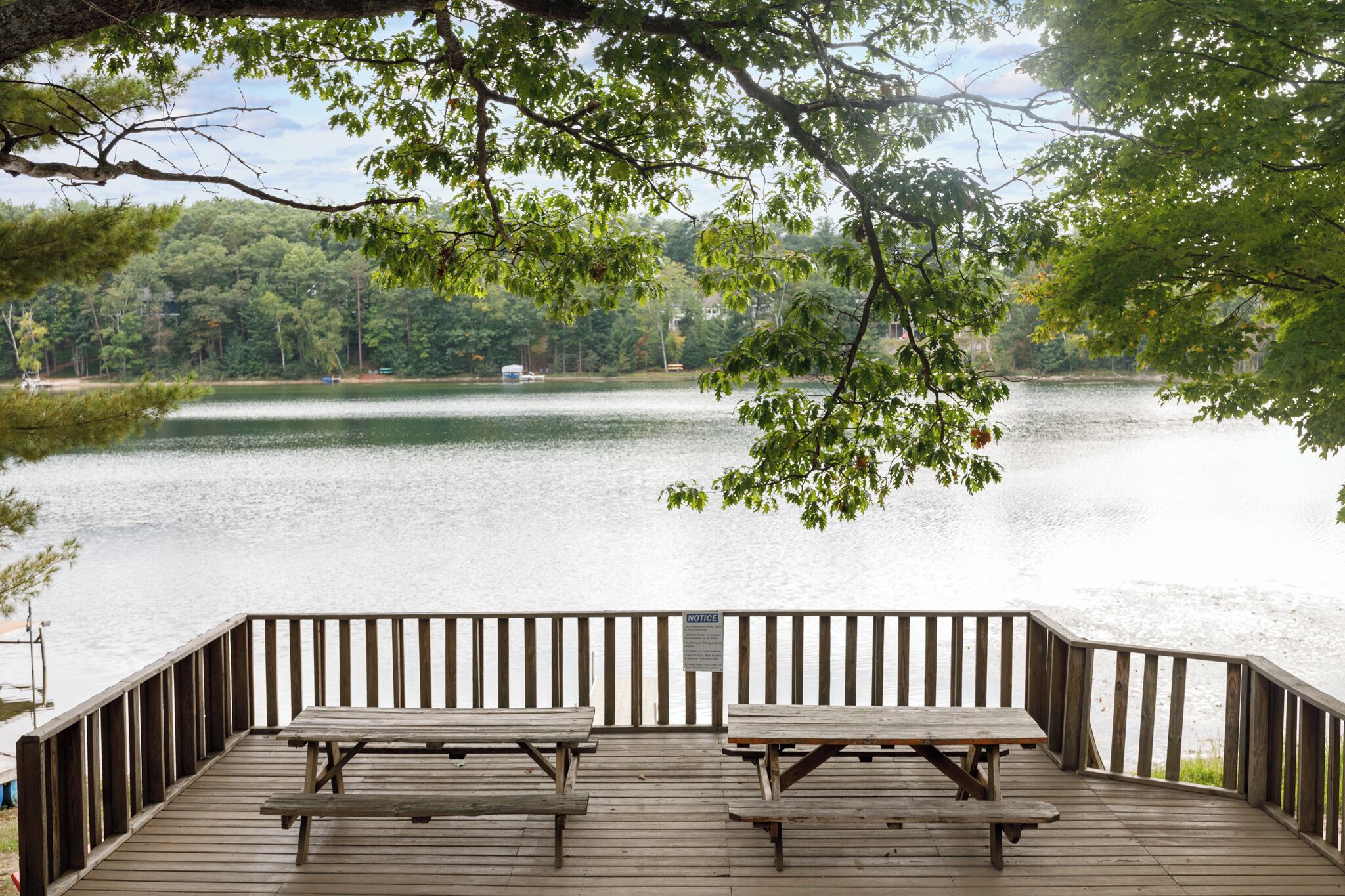 Een houten terras met picknicktafels met uitzicht op een meer, omgeven door bomen.