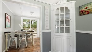 A dining area with a wooden table and chairs, a white cabinet with glass doors, and a view of the outdoors through a window. - Rennie Lake Hideaway (Traverse City)