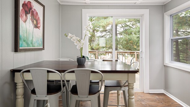 A dining area with a wooden table and white chairs, a framed painting, and a potted orchid. - Rennie Lake Hideaway (Traverse City)