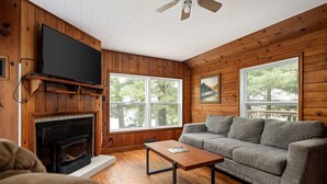 A cozy living room with a fireplace, a flat-screen TV, a gray sofa, and a wooden ceiling. - Rennie Lake Hideaway (Traverse City)