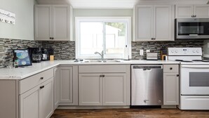 A modern kitchen with light gray cabinets, a stainless steel dishwasher, and a built-in oven. - Rennie Lake Hideaway (Traverse City)