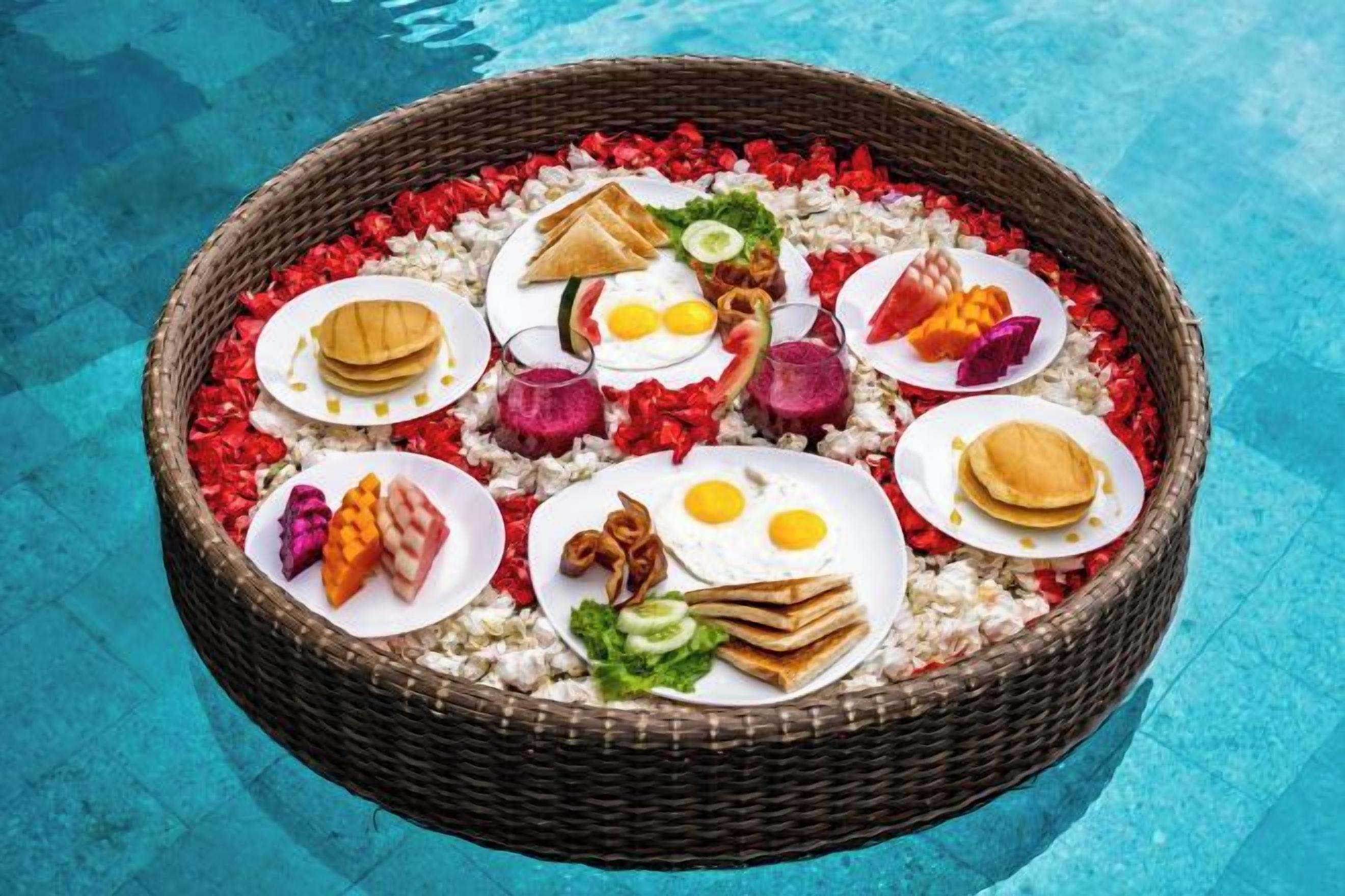 A round wicker basket filled with various food items placed on a poolside.