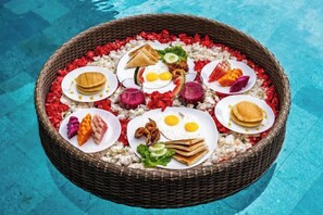 A round wicker basket filled with various food items placed on a poolside. - Villa Eden by BaliSuperHost (Bali)