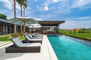 A swimming pool with lounge chairs and umbrellas, surrounded by a modern house and lush greenery. - Villa Eden by BaliSuperHost (Bali)
