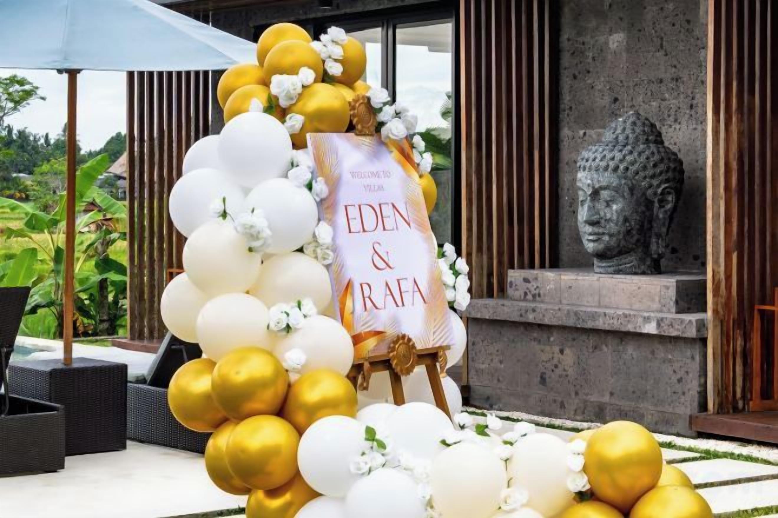 Une décoration festive comprenant une banderole aux couleurs d'Eden & RaFA, entourée de ballons blancs et dorés, avec une statue de Bouddha en arrière-plan.