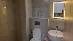A modern bathroom with a toilet, bidet, and sink. - Anantya Inn (Greater Noida)