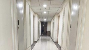 A long, narrow hallway with white walls and doors on both sides, leading to a dark doorway at the end. - Anantya Inn (Greater Noida)