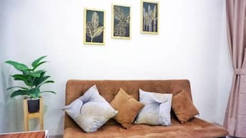 A brown sofa with three cushions, a small wooden stool with a plant, and two framed leaf artworks on the wall.