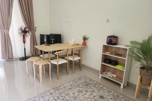 A dining area with a wooden table and chairs, a standing fan, a bookshelf, and a potted plant. - Baturu Villa Kayana Regency D9 (Junrejo)